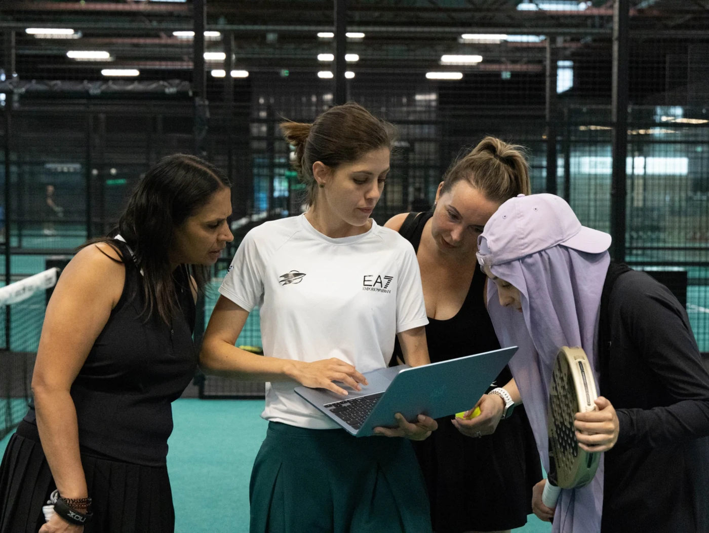 Four players looking at a laptop beside a padel court
