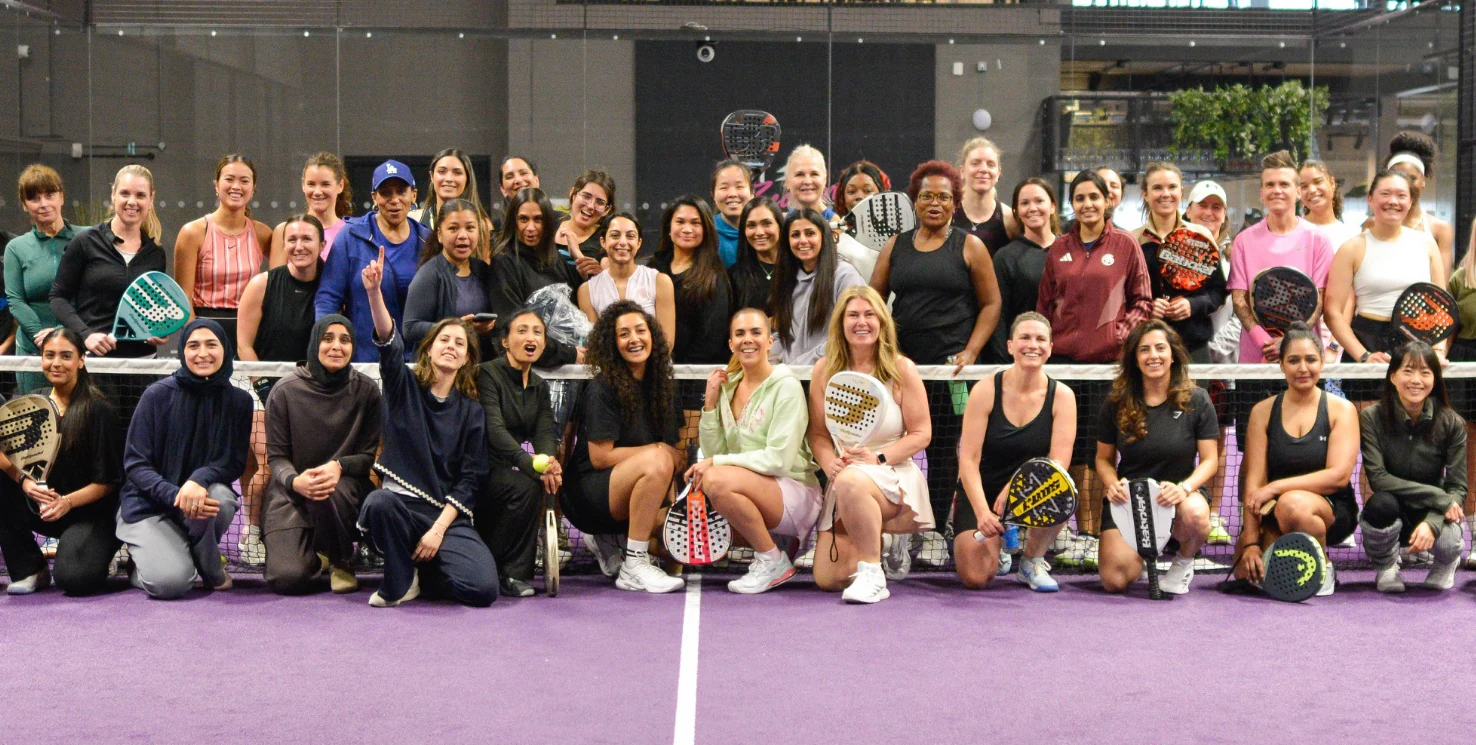 A large group of players smiling together on a purple indoor padel court